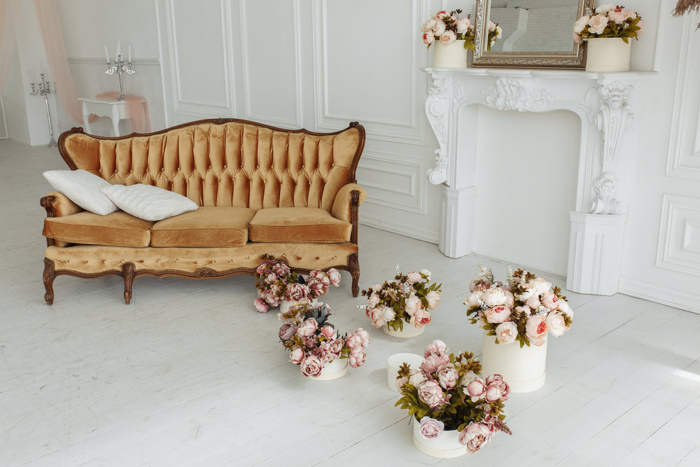 Espacio decorado al estilo cottage con un sofá vintage, chimenea ornamental y arreglos florales en tonos suaves. Una combinación de elementos rústicos y elegantes que evoca el encanto y la calidez de una casa de campo con estilo refinado.